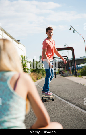 Rückansicht des Mädchens im Vordergrund und Teenager auf Skateboard im Hintergrund, Deutschland Stockfoto