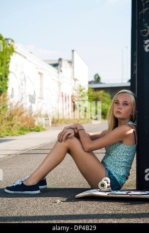 Porträt von Teenager-Mädchen im Freien mit Skateboard, Blick in die Ferne, sitzt auf der Straße, Deutschland Stockfoto