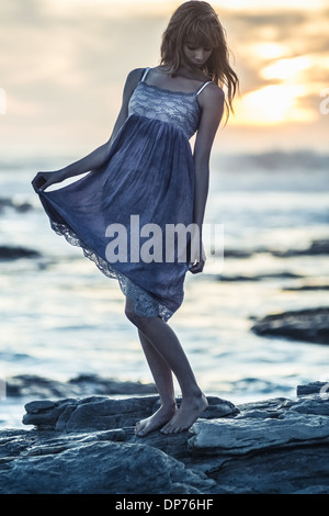 Schöne junge Frau, die auf Felsen am Meer Stockfoto