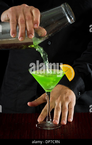 professionelle Barkeeper Gießen einen grünen Cocktail in einem Martini-Glas mit einer Orangenscheibe garnieren Stockfoto