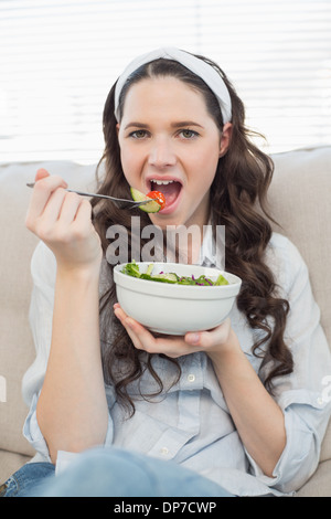 Wunderschöne lässige Frau auf der gemütlichen Couch essen Salat Stockfoto