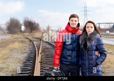 Junges Paar warten auf die Bahn verfolgt mit einem Koffer stand Arm in Arm, als sie die Ankunft des Zuges erwarten um ihren Urlaub zu beginnen. Stockfoto