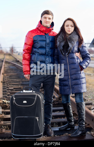 Junges Paar gehen Sie auf Urlaub stehen Arm in Arm mit ihren Koffer in der Mitte der Bahnstrecke auf Holzschwellen warten auf den Zug. Stockfoto