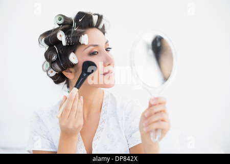 Hübsche Brünette in Lockenwickler halten Handspiegel und Schminken Stockfoto