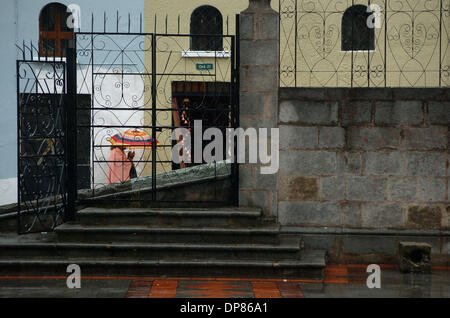 7. November 2006 - Quito, Ecuador - eine Frau in rosa gekleidet und trägt einen lebhaft gefärbten Regenschirm geht vorbei an schwarzen Metall und graue Pflastersteine, die das Tor zu der Basilika del Voto Nacional in Ecuadors Hauptstadt bilden. Auf einem kleinen Hügel in der Altstadt Quitos und sichtbar von einem Großteil der Stadt befindet, sich die neugotische Kirche, gebaut im Jahre 1892 eines der ältesten kolonialen build Stockfoto