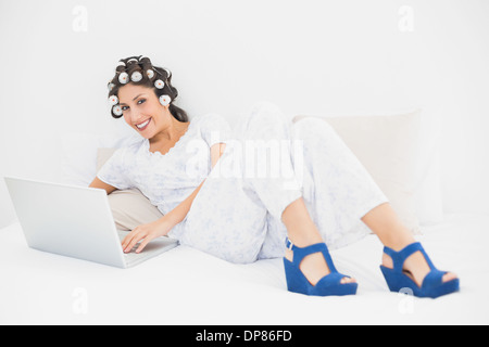 Brünette in Lockenwickler und Keil Schuhe mit ihrem Laptop auf Bett Stockfoto