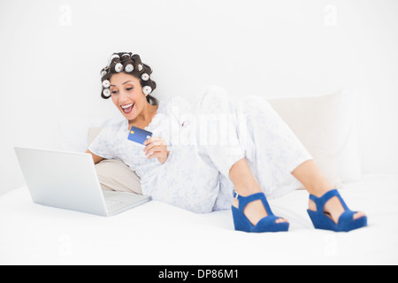 Aufgeregt Brünette in Lockenwickler und Keil Schuhe mit ihrem Laptop für Online-shopping Stockfoto