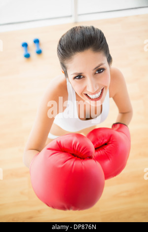 Fit Frau trägt rote Boxhandschuhe lächelnd in die Kamera Stockfoto