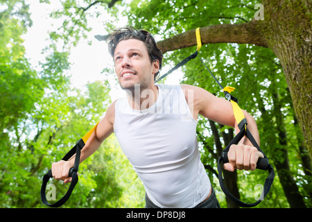 Mann mit Suspension Trainer Schlinge im Stadtpark unter Sommer Bäume für Sport Fitness Training Stockfoto