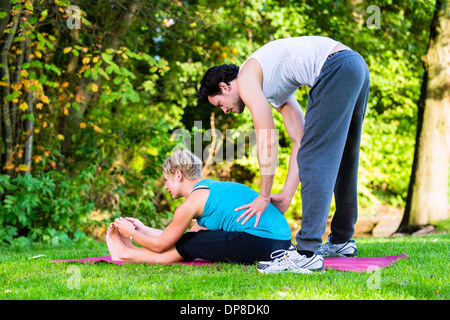 Junge Frau im Stadtpark Yoga machen oder Aufwärmen für das Training mit ihrem persönlichen Trainer oder Lehrer Stockfoto