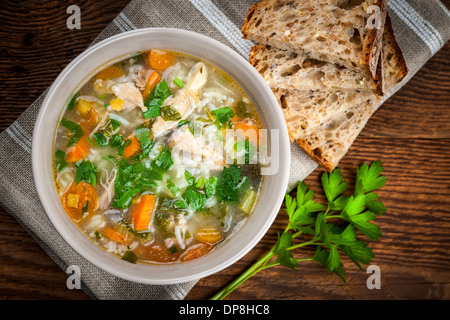 Huhn-Reis-Suppe mit Gemüse in Schüssel und Brot von oben Stockfoto