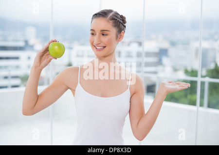 Lächelnde sportliche Brünette hält grüne gesunde Apfel Stockfoto