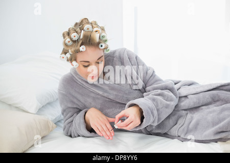 Konzentriert entspannte blonde Frau in Lockenwicklern Nagellack auftragen Stockfoto