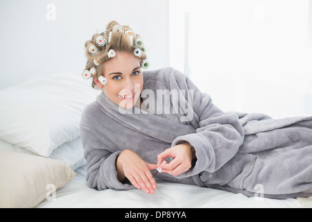 Freuen uns entspannt blonde Frau in Lockenwicklern Nagellack auftragen Stockfoto