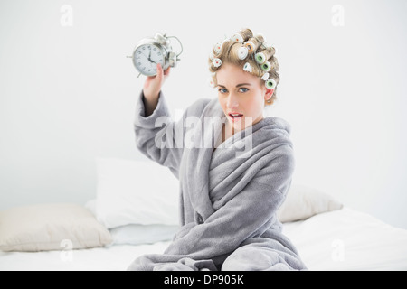 Böse blonde Frau in Lockenwicklern werfen ihr Wecker Stockfoto