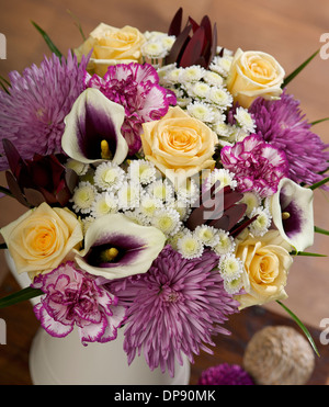 Weisser Hengst Chrysanthemen, purpurrote umrandete Spray Nelken, kastanienbraun Leucadendron, lila Calla Lilien und Avalanche Rosen in einer Vase in einer häuslichen Umgebung Stockfoto