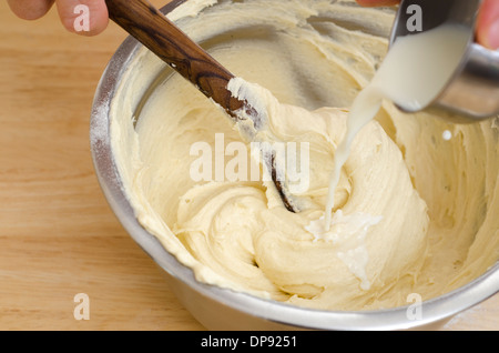 Mit Holzlöffel mischen Hände Kuchen Zutaten unter Rühren Milch hinzufügen. Stockfoto