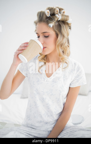 Friedliche hübsche Blondine trägt Lockenwickler Kaffeetrinken Stockfoto