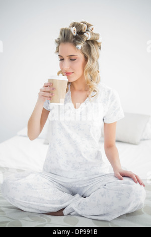 Friedliche hübsche Blondine trägt Lockenwickler duftenden Kaffee Stockfoto