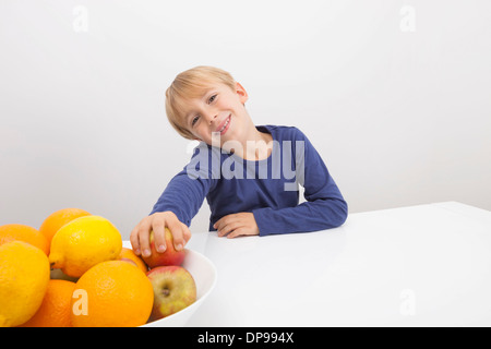 Porträt eines jungen hält Apfel aus der Obstschale am Tisch Stockfoto