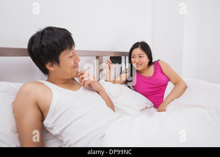 Asiatische Frau, die eine Aufnahme des Mannes mit Handy im Bett Stockfoto