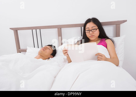 Junge Asiatin Buch von Mann schlafend im Bett Stockfoto