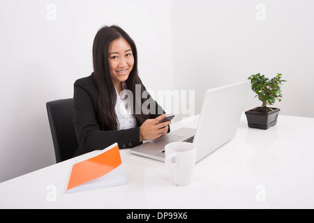 Porträt von lächelnden Geschäftsfrau mit Handy am Schreibtisch Stockfoto