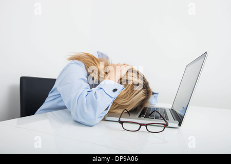 Müde Geschäftsfrau ruhen Kopf auf Laptop im Büro Stockfoto