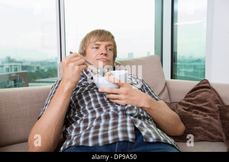 Entspannte Mitte erwachsener Mann mit Schüssel Müsli im Wohnzimmer zu Hause Stockfoto