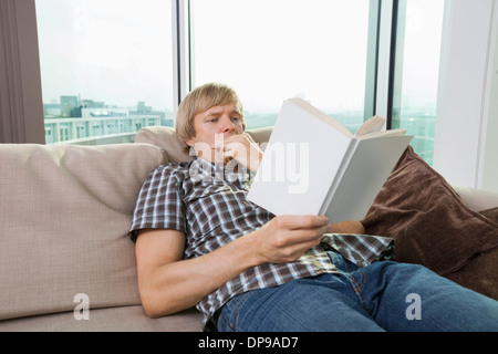 Entspannte Mitte erwachsener Mann Lesebuch im Wohnzimmer zu Hause Stockfoto
