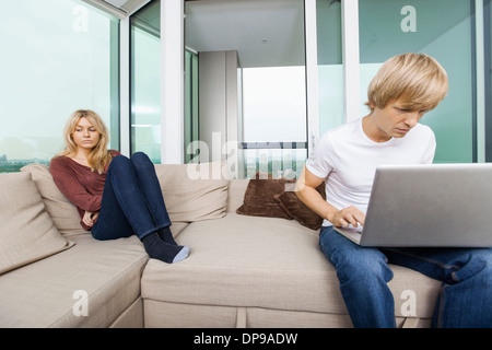 Traurige Frau neben Mann mit Laptop im Wohnzimmer zu Hause Stockfoto
