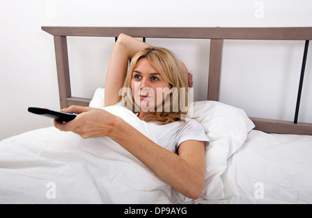 Junge Frau Senderwechsel mit Fernbedienung im Bett Stockfoto