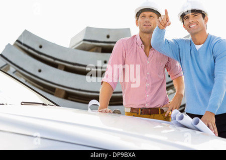 Architekten mit Blaupausen auf Auto diskutieren auf Baustelle Stockfoto