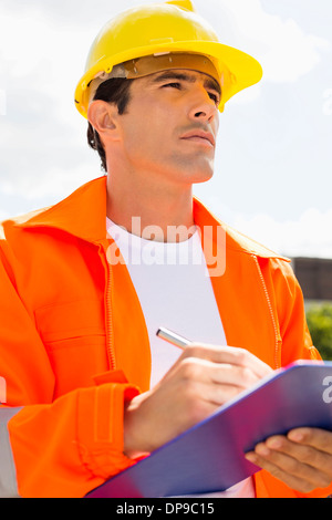 Männlichen Bauarbeiter mit Zwischenablage wegsehen außerhalb Stockfoto