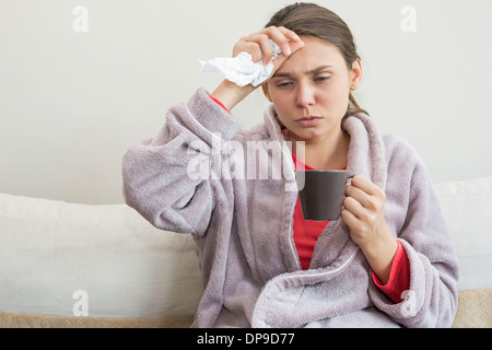 Junge Frau leidet Kälte Kaffeetrinken auf Bett Stockfoto