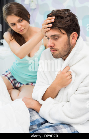 Junge Frau, die Überprüfung des Mannes Temperatur auf Bett Stockfoto