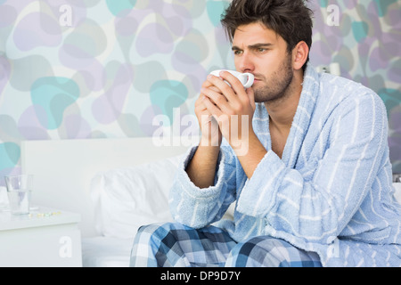 Kranker Mann sitzend auf Bett zu Hause Kaffee trinken Stockfoto