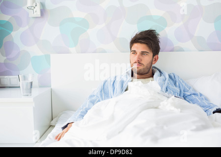 Kranker Mann mit Thermometer im Mund liegend auf dem Bett zu Hause Stockfoto