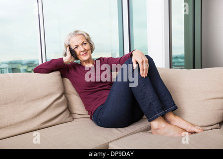 Full-length senior Frau Beantwortung Smartphone zu Hause auf sofa Stockfoto