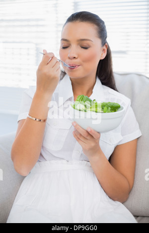 Entspannte hübsche Frau essen gesunde Salat auf sofa Stockfoto