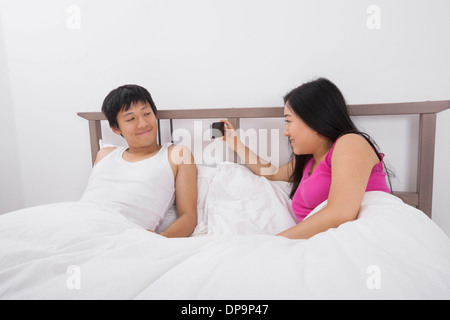 Asiatische Frau, die eine Aufnahme des Mannes mit Handy im Bett Stockfoto