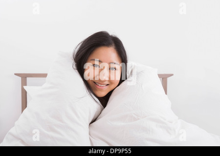 Porträt der glückliche Frau eingewickelt in Quilt auf Bett Stockfoto