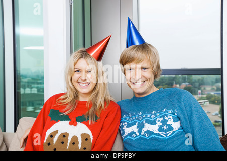 Porträt von fröhlich paar tragen Weihnachtspullover und Partyhüte im Wohnzimmer zu Hause Stockfoto