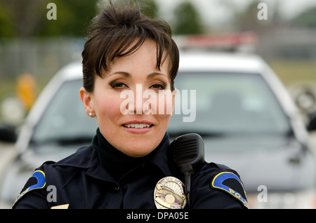 eine freundlich und lächelnd Hispanic Polizistin mit ihrem Streifenwagen. Stockfoto