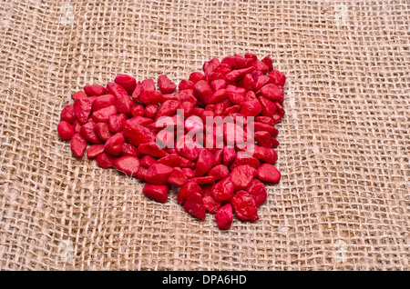 Rotes Herz gemacht von dekorativen Steinen auf einem Hanf-Hintergrund Stockfoto