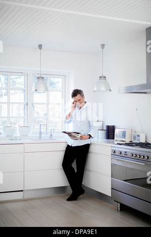 Mann steht in der Küche-Anruf tätigen und Zeitung lesen Stockfoto