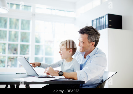 Mann, sitzend am Schreibtisch mit Sohn auf seinem Knie mit Laptop-Computer und Unterlagen Stockfoto