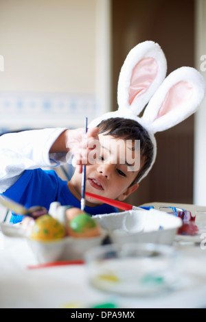 Jungen tragen Hasenohren bemalen von Ostereiern Stockfoto