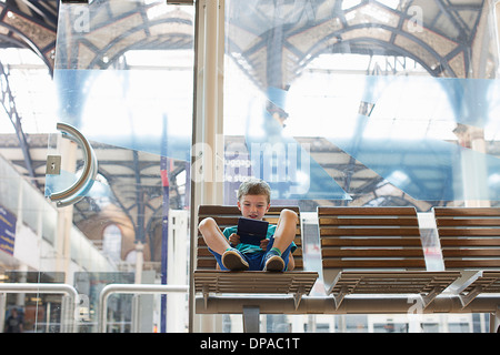 Kleiner Junge im Zug Bahnhof Wartezimmer Handheld-Spiel Stockfoto