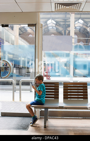 Kleiner Junge im Zug Bahnhof Wartezimmer elektronisches Spiel Stockfoto